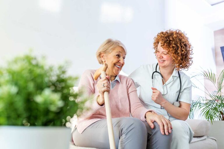 Two elderly residents and a caregiver washing hands together at a sink in a bright, clean assisted living facility.